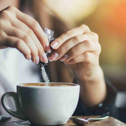 A person filling a cup of coffee with a sweetener powder